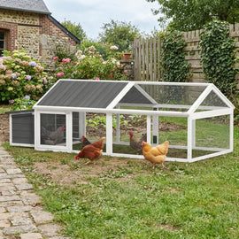 Le parc couvert installé dans un jardin, trois poules rousses devant une maison en pierre