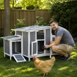 Poulailler en bois gris et blanc surélevé, un homme et une poule devant